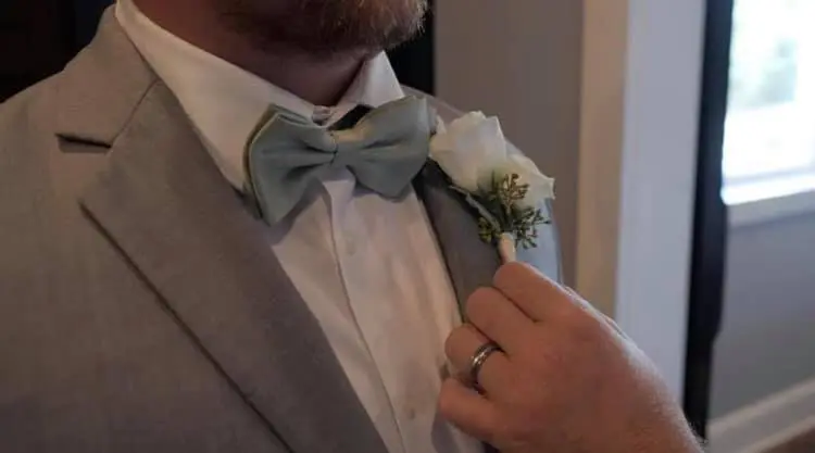 a white boutonnière being pinned to a the lapel of a man's gray tuxedo coat