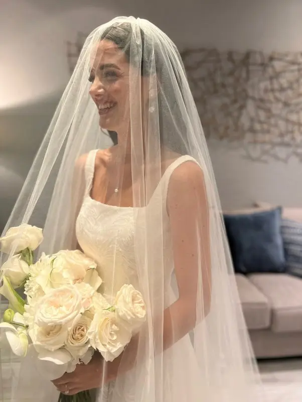 bride holding a creamy white flower bouquet smiles under her veil