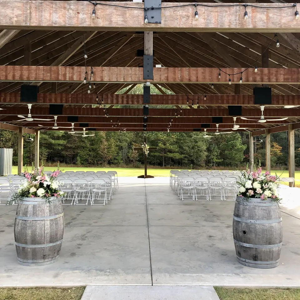 floral arrangements atop barrels under wooden pavilion 