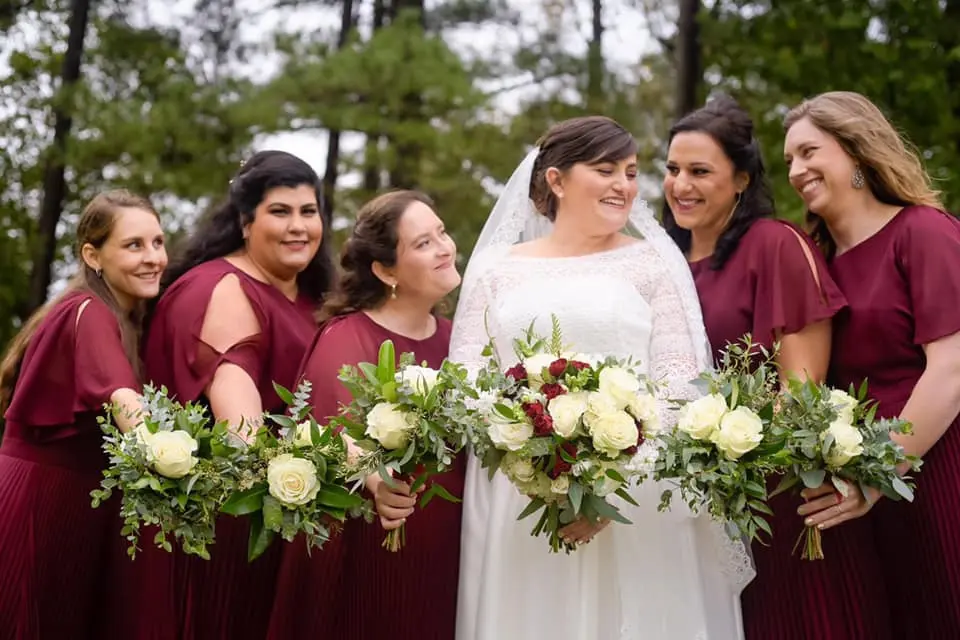 bride in white and bridesmaids in burgundy, holding coordinating floral bouquets